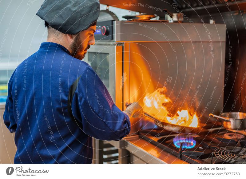Chef cooking with flame in frying pan chef work kitchen fire dish man professional flambe hot stove gas prepare uniform hat adult occupation commercial male