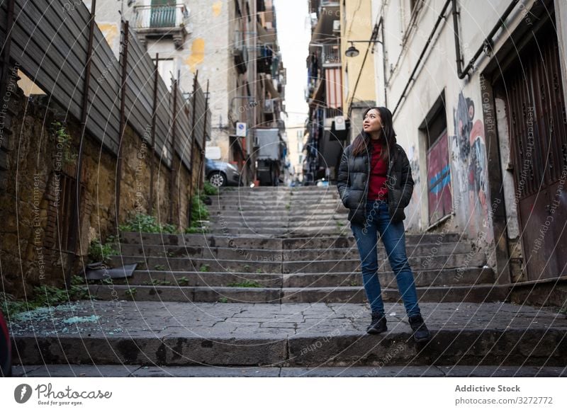 Ethnic woman standing on steps on shabby street building ethnic exterior city hands in pockets lifestyle female rest relax cool weathered district area ghetto
