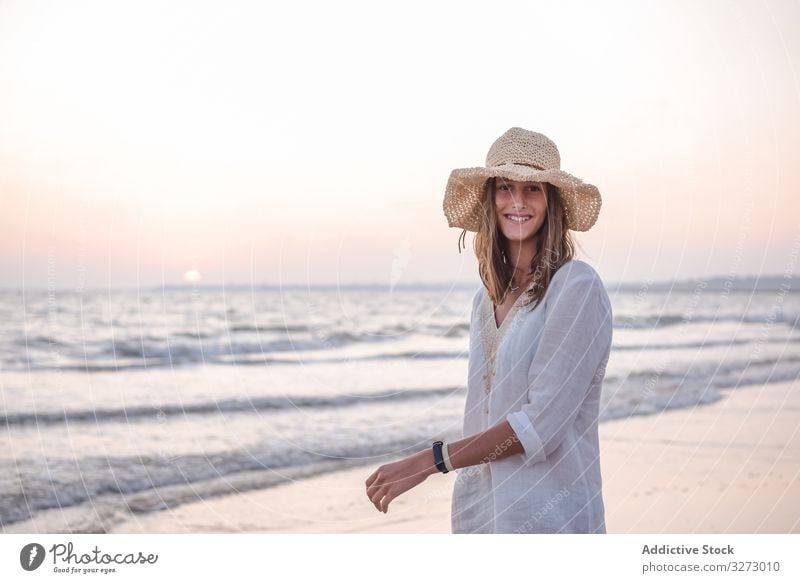 Charming woman in light white dress on wavy beach sea traveling seaside tourism charming vacation hat curly holiday summer freedom journey young relaxing