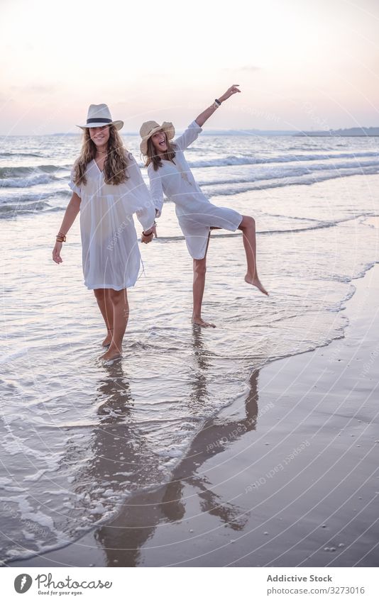 Smiling girlfriends in summer clothes barefoot in water on beach women sea traveling seaside charming vacation hat curly holiday together freedom journey female