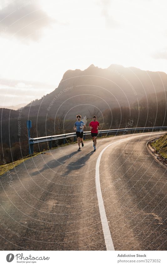 Sportsmen running on asphalt road in mountains sportive nature active jogger training together hill cross country curve path way male sportsmen morning friend