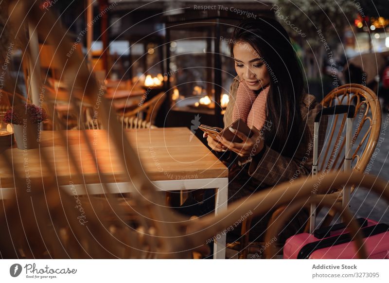 Asian traveler using smartphone in cafe woman tourist suitcase ethnic evening city urban female asian browsing social media casual smile cheerful glad
