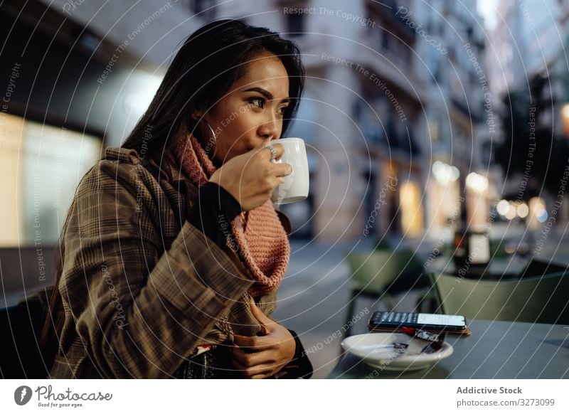 Asian woman enjoying hot beverage in street cafe drink evening city urban sip cup ethnic female young stylish trendy coffee tea lifestyle rest relax lady asian