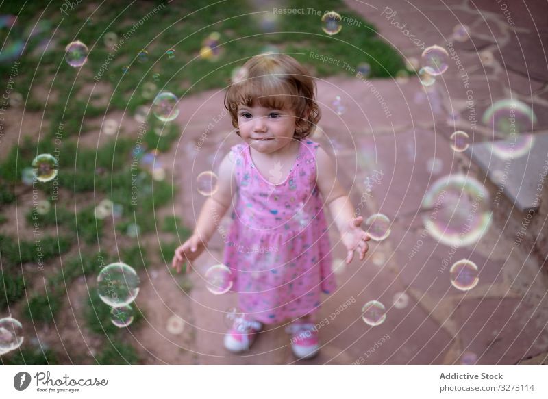 Joyful girl playing with colorful bubbles in grass soap childhood joyful fun adorable cheerful park playful enjoyment action wet little motion recreational blow