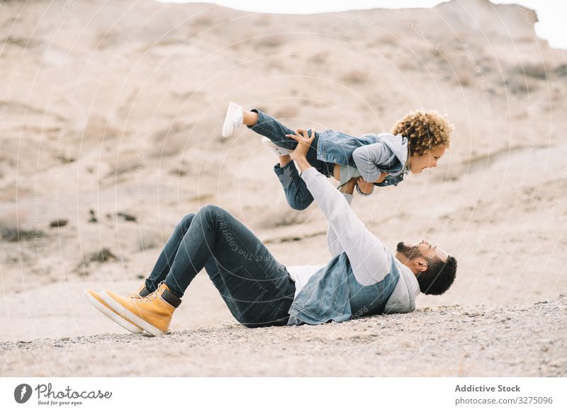 Ethnic father playing with child on ground toddler fun rest sand hill smile parent happy cheerful lifestyle modern nature dad man horizontal bonding love tender