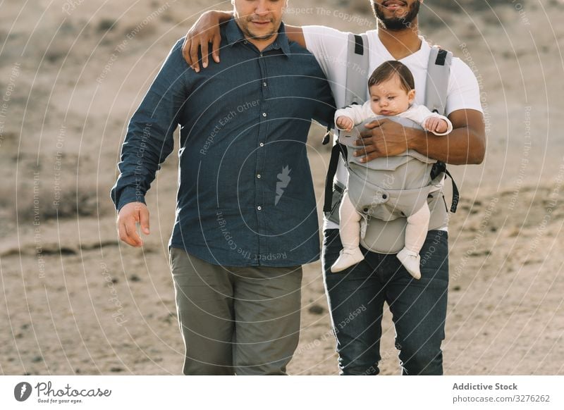 Unrecognizable diverse men walking with baby on nature gay together carrier support cuddle generation interaction lgbt homosexual stroll father male child