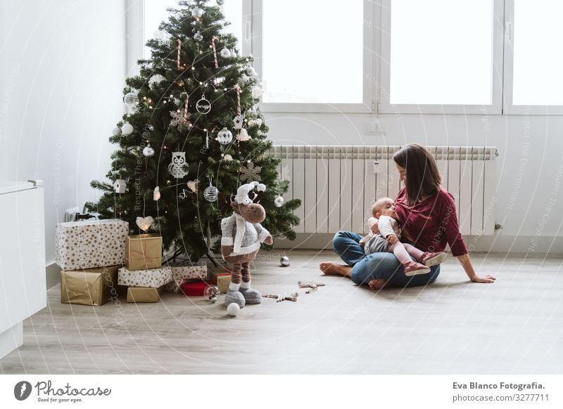 mother breastfeeding her baby girl by the Christmas tree Appease To feed Eating Natural Food Mother motherhood Happy Cute Baby Girl one year decorating