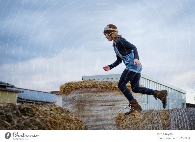 Girl jumps over bale of straw Playing Adventure Farm Child 1 Human being 3 - 8 years Infancy Nature Straw Bale of straw Cap Jump Athletic Happiness Fresh Happy