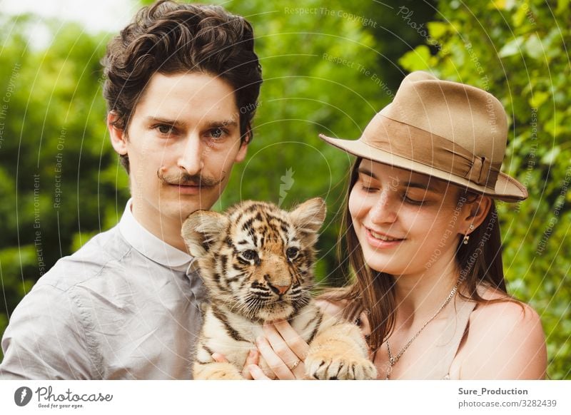 A man and woman hold tiger cub angry animal background bengal black cat close closeup eater face forest friend glamour hat head hunter jungle macho mustche