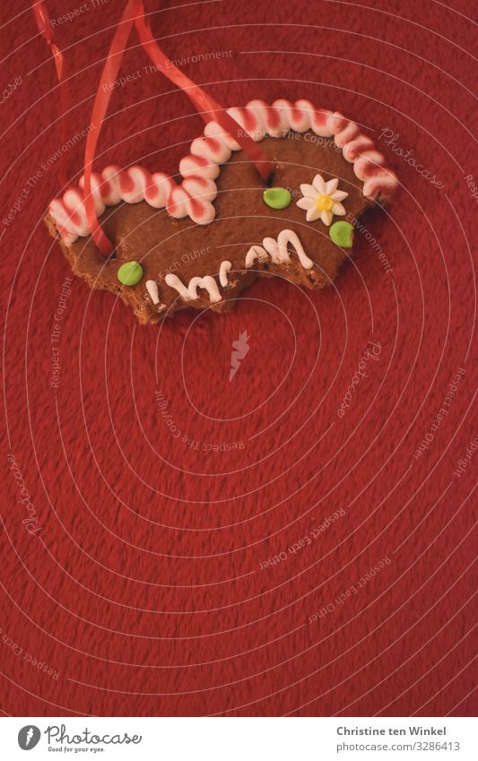 bite into gingerbread heart on red background Food Dough Baked goods Gingerbread heart Nutrition Kitsch Odds and ends Souvenir Heart Happiness Hip & trendy