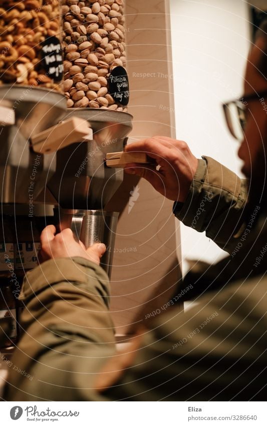 A man filling nuts from a container in a packaging-free supermarket; sustainability Masculine Shopping package-free unpacked Without Packaging