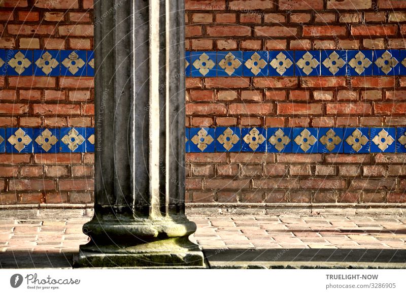Part of a neo-Byzantine style arcade with fluted column in front of yellowish-orange brick masonry horizontally banded with blue glazed, yellow patterned tiles