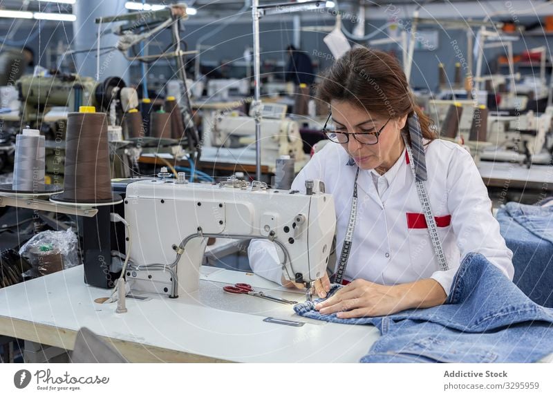 Woman's hands in textile factory sewing on industrial sewing machine. industry clothing manufacturing worker woman fabric pants blue jeans occupation production
