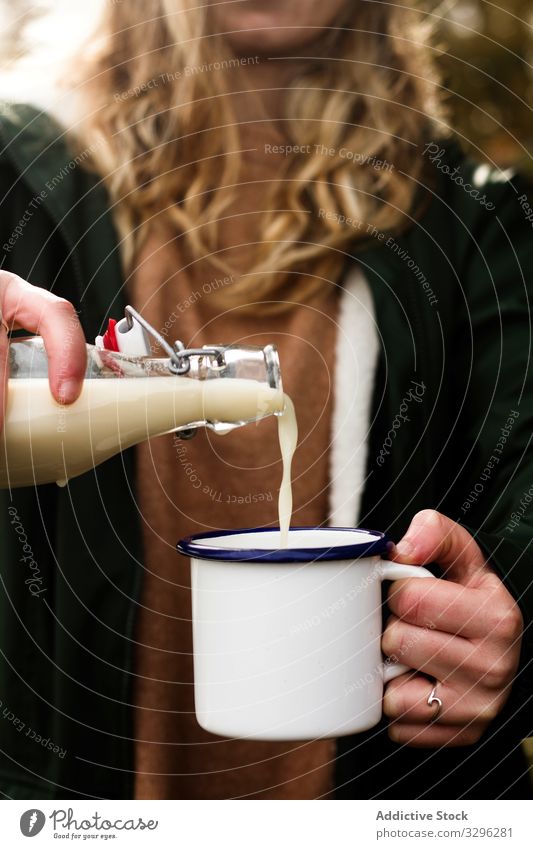 Woman pouring fresh milk from bottle to enamel mug while having refreshment in garden woman food hand beverage picnic lactose dairy drink healthy edible natural