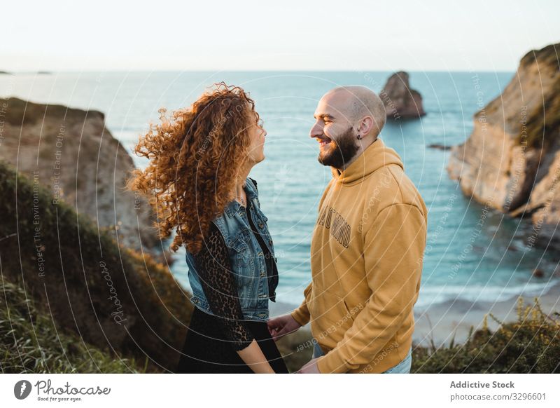 Cheerful couple in love standing at seaside romantic seashore happy ocean rock cliff nature hipster seascape young together talk coast water romance