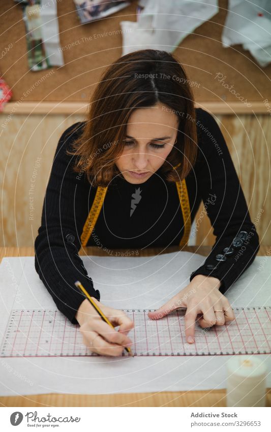 Female tailor drawing cutout in workshop woman table focused adult designer workplace professional workspace female pencil measure fashion small business job