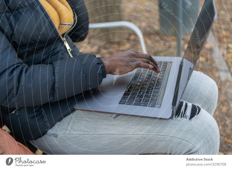 Smart smiling black long haired woman typing on laptop sitting on bench in park leaves female working using gadget nature stylish african american natural