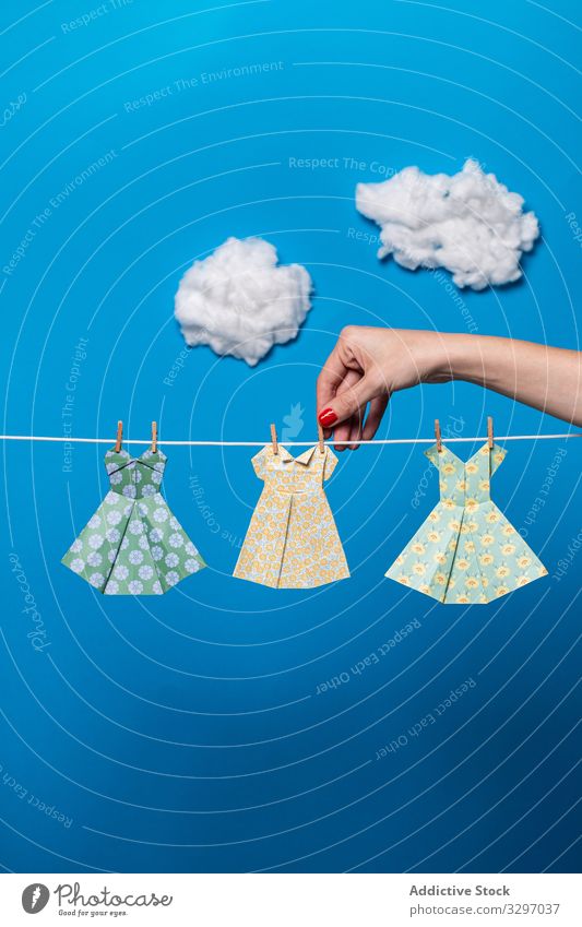 Crop woman attaching origami dresses to rope concept hang clean laundry sky cloud female bright vivid vibrant paper mockup creative art craft lady apparel