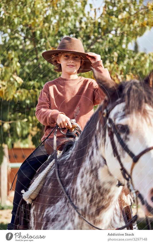 Boy in hat riding his brown mottled horse child rider summertime leisure countryside caucasian vacation horse riding thoroughbred helmet 8-9 years lifestyle boy
