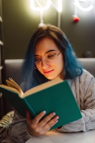 Young adult mixed asian female with blue hair holding a book in a cafe with neon lights, selective focus Beauty Photography Book Café colorful hair Face Woman