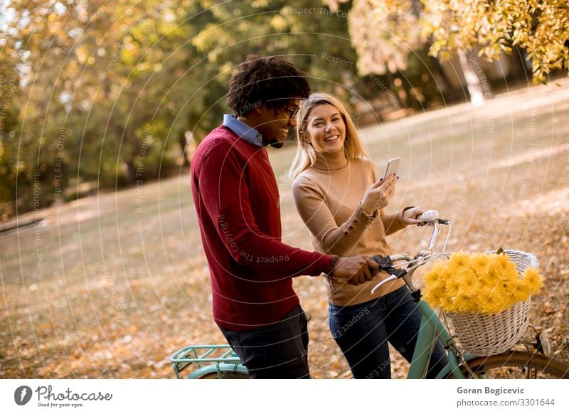 Multiracial couple with bicycle standing in the autumn park Lifestyle Happy Beautiful Leisure and hobbies Telephone PDA Woman Adults Man Couple Autumn Flower