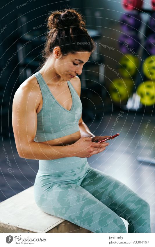 Fitness woman consulting her training on her smartphone sitting in a jump box in the gym Lifestyle Body Music Club Disco Sports Telephone PDA Technology