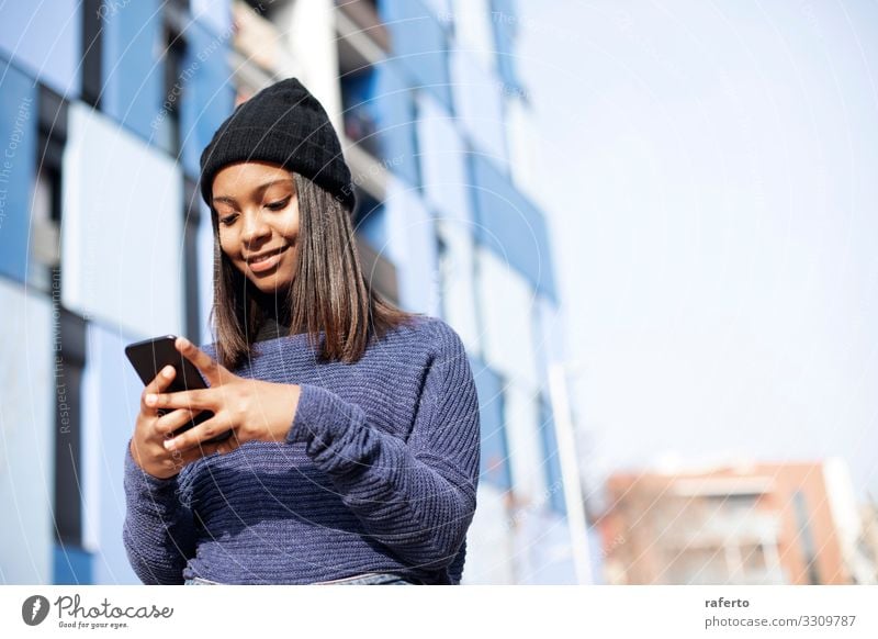 Portrait of African American young woman wearing a wool cap standing on the street while using a mobile phone Lifestyle Happy Beautiful Telephone PDA Technology