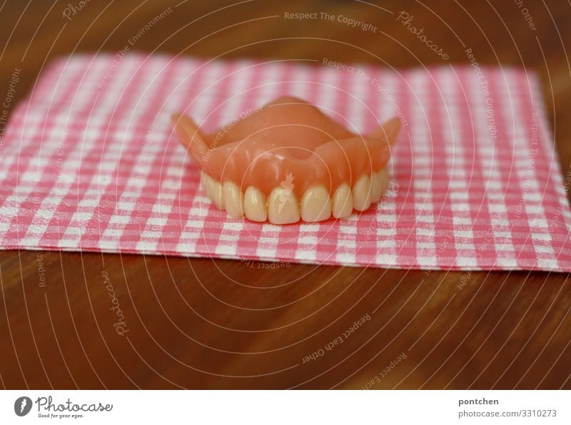 Dental health. Dentures of the upper teeth are lying on a pink and white chequered cloth Dentist Uniqueness Funny Teeth Checkered Half Pink Napkin