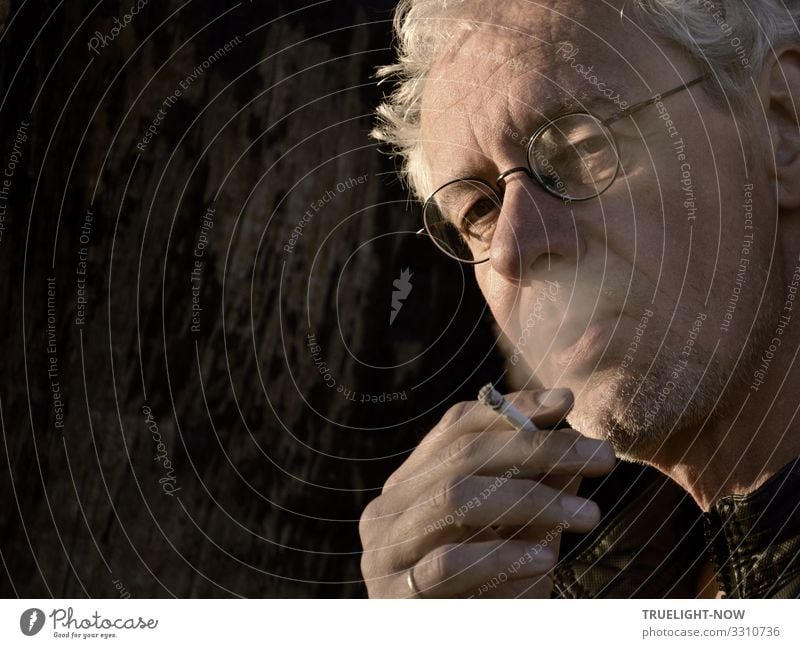 White-haired, smoking man with glasses and a critical look, burning cigarette in his hand, ring on his little finger, illuminated by the evening sun in front of a dark background, photographed in a cropped half-profile, under-sighted