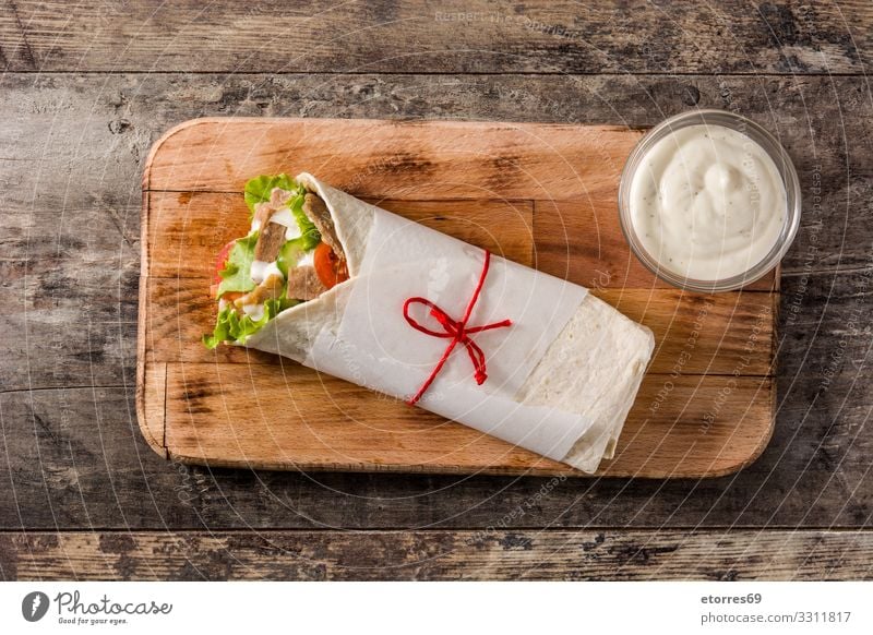 Doner kebab or shawarma sandwich on wooden table. doner Kebab Sandwich Wrap Meat Roll Chicken Vegetable Tomato Lettuce Onion Herbs and spices Sauce Greek gyros