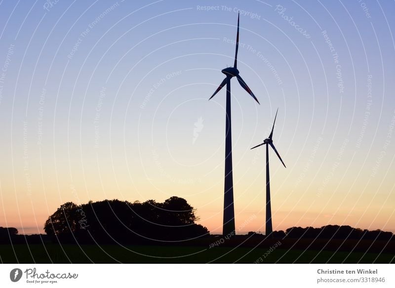 Two wind turbines at sunset / sunrise Wind energy plant Technology Advancement Future Climate Neutral Energy industry Renewable energy Cloudless sky Innovative