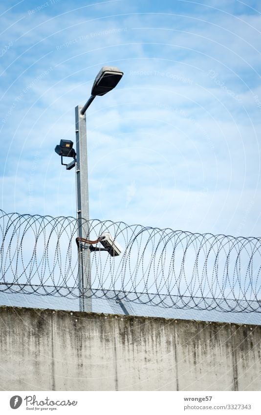 Surveillance camera on a light pole behind a wall with barbed wire Wall (barrier) Concrete wall Barbed wire Light pole Floodlight Spotlight Wall (building)