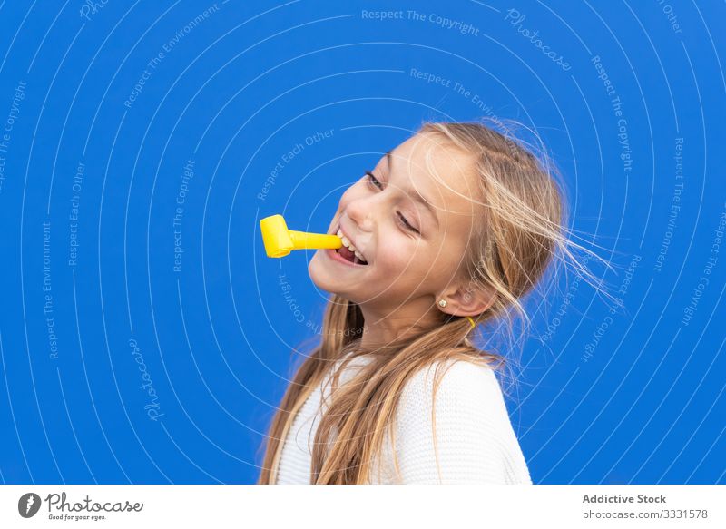 Content girl playing with party horn fun cheerful birthday yellow kid smile laugh casual childhood carefree happiness beautiful female festive game activity
