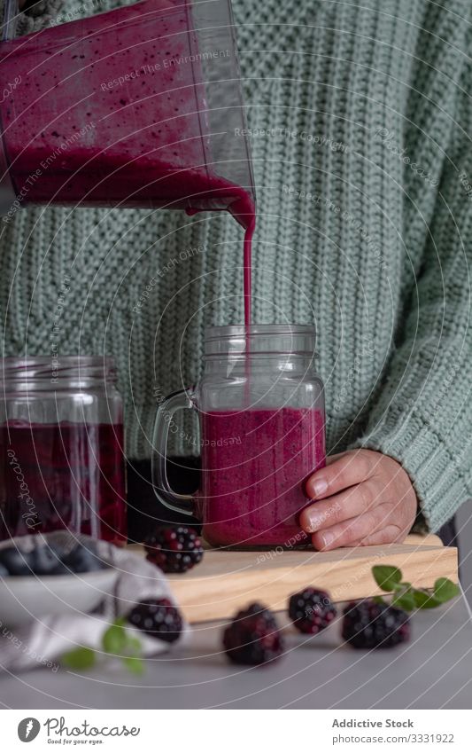 Cook pouring tasty healthy drink of berry mix and mint from blender into transparent jug in contemporary kitchen smoothie fruit jar hand detox fresh food