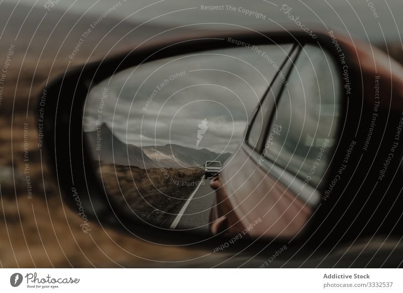 Car moving on asphalt marked road and reflecting in mirror of front car under gray sky reflection hill mountain travel nature landscape racing tourism adventure