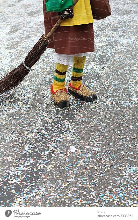 Two legs stand in brown straw shoes and robe, disguise, dress, apron, broom, witches broom, straw broom disguised as a witch on the street covered with confetti, at carnival at a carnival parade, the traditional Buernfasnacht in South Baden.