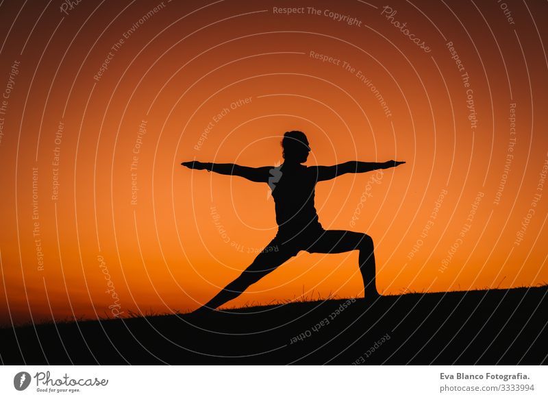 silhouette of young man in a park doing yoga sport. orange sky background. healthy lifestyle. Silhouette Back-light Concentrate Position Human being