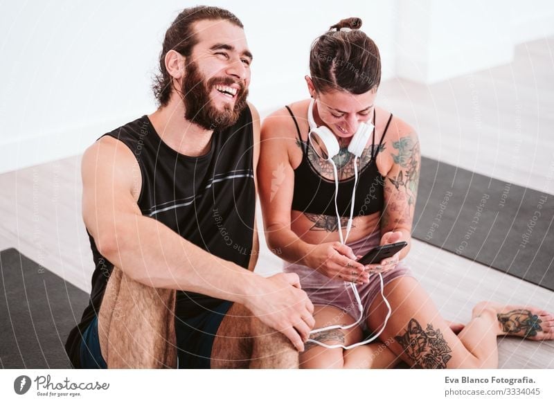 two friends at the gym listening to music on mobile phone and headset and having fun. Sport and technology concept Couple Friendship Youth (Young adults) Man