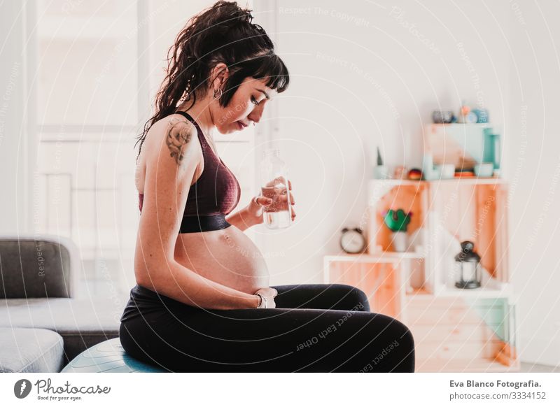 young pregnant woman at home sitting on pilates ball, drinking water. healthy lifestyle Pregnant Woman Yoga Home Sports Healthy Lifestyle Youth (Young adults)
