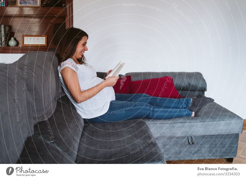 young pregnant woman at home reading a book Pregnant Woman Youth (Young adults) pregnancy Reading Book Home maternity Life Lounge Showing one's bellybutton