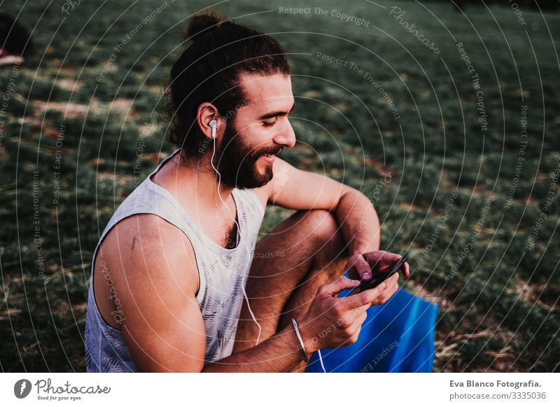 young man in a park listening to music on mobile phone and headset after practicing yoga sport. city background. healthy lifestyle. Music Cellphone Technology