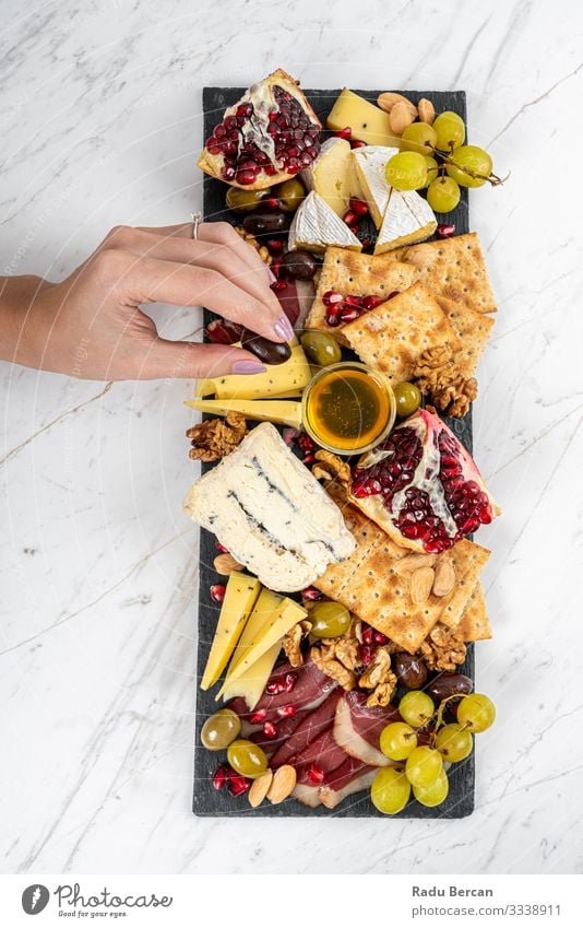 Food Platter With Truffle Cheese, Duck Breast, Brie Cheese, Pecan Nuts, Pomegranate Seeds, Grapes, Almonds, Honey, Olives and Crackers on White Marble Background