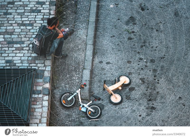 play street Masculine 1 Human being Town Traffic infrastructure Street Lie Sit Blue Yellow Gray Kiddy bike Asphalt Colour photo Subdued colour Exterior shot
