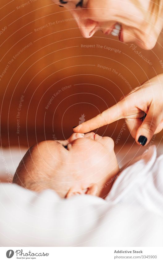 Bright mother touching nose by nose of baby play happy bonding care newborn affection lying bed home infant open mouth adorable leisure child small cute kid