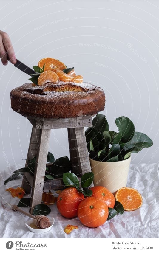 Person pouring sugar powder with tea strainer above cake tangerine citrus still life fruit stool dessert orange sweet mandarin pastry gourmet delicious wooden