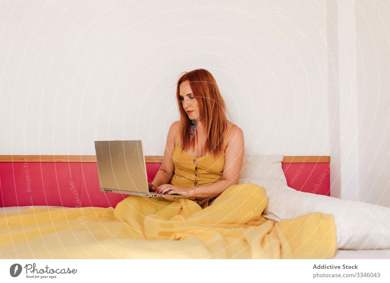 Woman working laptop on bed at home woman using browsing freelance lying morning busy smart yellow gown dress female lifestyle young internet sitting online