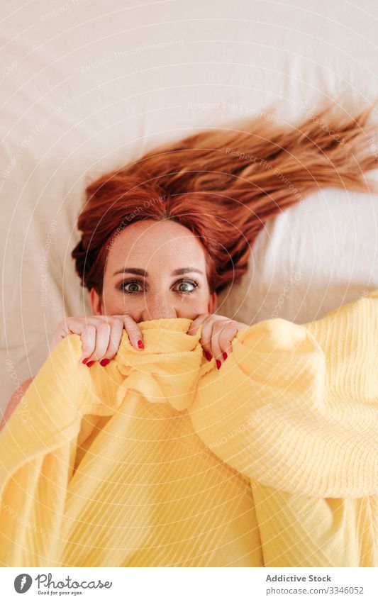 Positive lady hiding under blanket at home woman lying bed morning sitting cover yellow fun relax rest smile enjoy playful redhead lifestyle young beautiful