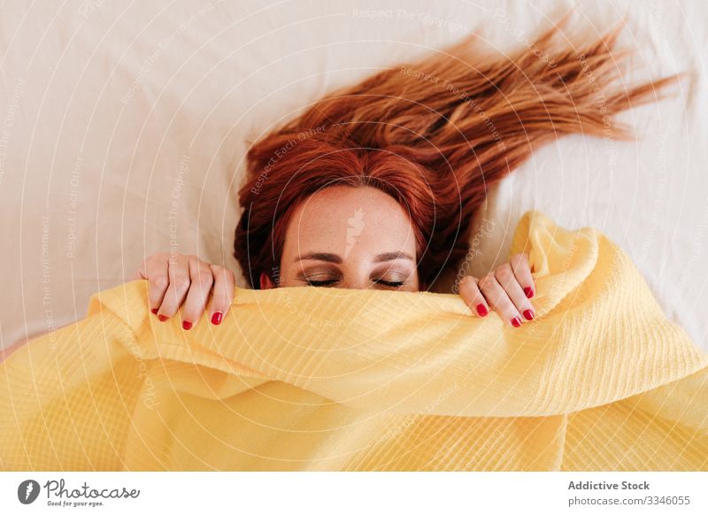 Positive lady hiding under blanket at home woman lying bed morning sitting cover yellow fun relax rest smile enjoy playful redhead lifestyle young beautiful