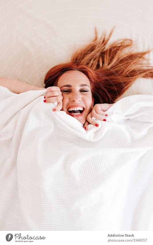 Positive lady hiding under blanket at home woman lying bed morning sitting cover fun relax rest smile enjoy playful redhead lifestyle young beautiful female