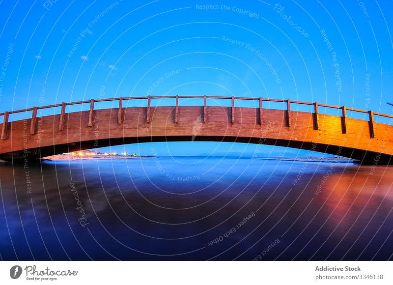 Wooden bridge extending in arc over flat surface of water under blue sky cityscape reflection river architecture travel skyline scenic urban scene tourism